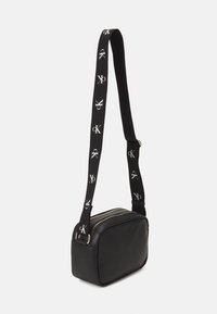 Borsa a tracolla sintetica nera con chiusura a zip, forma rettangolare piatta e una tracolla a contrasto con motivi del logo ripetuti.