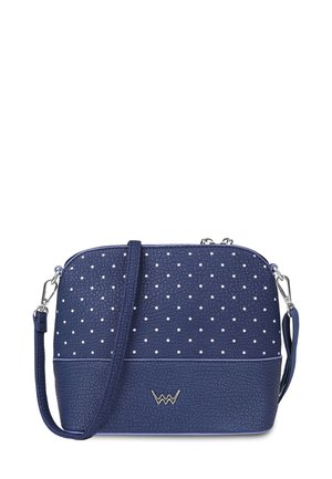 Navy blue crossbody bag in textured synthetic material, featuring white polka dots and silver hardware, with an adjustable strap and logo detail.