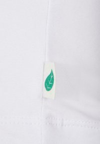 Hvid bomuldsstof med en søm og et synligt mærke med et grønt blad-design, der angiver økologisk materiale.