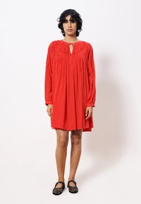 Rotes, langärmliges Kleid mit einem Schlüssellochausschnitt und gerafften Details an der Brust; leichtes Material mit einer fließenden Silhouette.