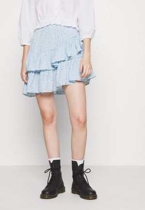 Person wearing a white blouse, light blue ruffled skirt with eyelet pattern, white socks, and black lace-up combat boots against a plain background.