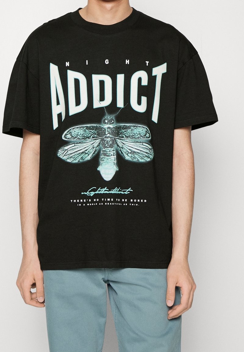 Černé bavlněné tričko s velkým tyrkysovým grafickým motivem můry a silným nápisem "NIGHT ADDICT" nahoře a sloganem dole. Uvolněný střih.