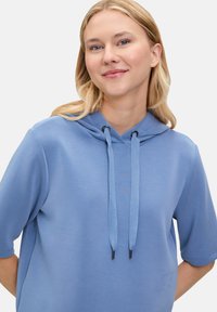 Jasnoniebieska bluza z kapturem wykonana z miękkiego materiału, z kapturem na sznurku, krótkimi rękawami i luźnym krojem. Bez wyraźnych wzorów ani akcentów.