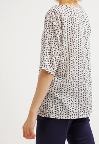 Top a maniche corte in tessuto leggero, presenta un motivo geometrico in blu, beige e bianco. Vestibilità rilassata con scollatura rotonda.