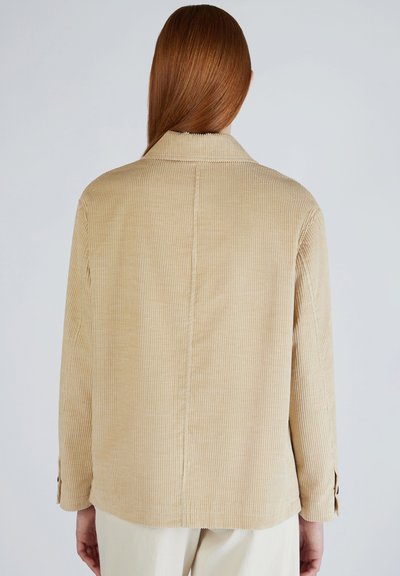 Giacca in corduroy beige con righe verticali, colletto e maniche lunghe. Presenta polsini con bottoni e un design semplice e pulito.