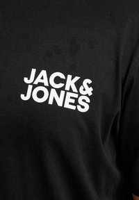 Schwarzes Baumwoll-T-Shirt mit großen weißen Buchstaben "JACK&JONES" in einer fetten, modernen Schriftart. Glatte Textur mit minimalen Details.