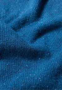 Közelkép texturált kék kötött szövet részleteiről, melyen kis színfoltok találhatók különböző színekben, és jól látható a szövés mintája.