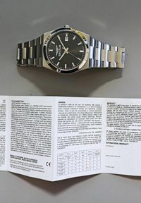 Orologio Sector con quadrante nero, cassa e bracciale in acciaio inossidabile argento, finestra per la data, indici delle ore argentati e dettagli rossi. Manuale di garanzia visibile.