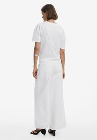 Hvid oversized t-shirt med korte ærmer, parret med hvide bukser med vidde, der har baglommer, og sorte hælede sandaler.