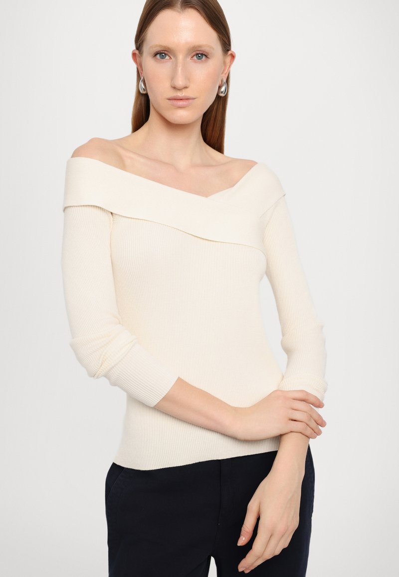 Cremfarbener, schulterfreier, gerippter Strickpullover mit langen Ärmeln und V-Ausschnitt. Figurbetonter Schnitt mit subtiler Textur.