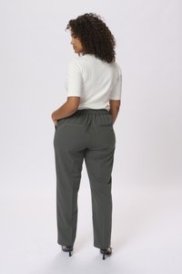 Top corto bianco a maniche corte, pantaloni verde con vita elastica e tasche, texture liscia, design a gamba dritta, scarpe nere con tacco.