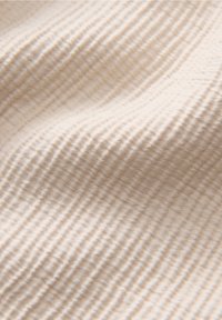 Tissu beige avec de fines stries horizontales régulièrement espacées, créant une surface douce et texturée avec des plis délicats.