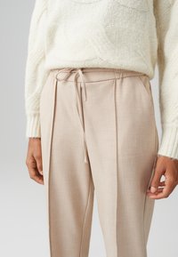 Beige op maat gemaakte broek met een trekkoord in de taille, met plooien, gecombineerd met een geweven crèmekleurige trui. Zachte, lichtgewicht stof.