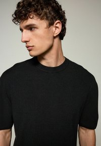 Sort kortærmet t-shirt med rund hals, ribbet tekstur, tætsiddende design, letvægtsstof, ingen synlige mønstre eller accenter.