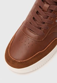 Braune Leder-Sneaker mit Wildlederakzenten, strukturiertem Obermaterial, perforiertem Design an der Spitze und passenden braunen Schnürsenkeln; weiße Gummisohle.