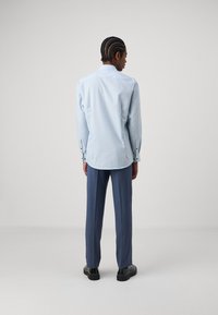Lichtblauw geruit overhemd met een spread collar, gecombineerd met donkere, op maat gemaakte blauwe pantalon en zwarte schoenen, bekeken vanuit de achterkant.