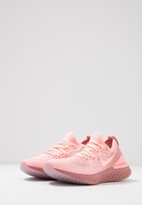 Svetle růžové sportovní boty s prodyšným pleteným svrškem, strukturovanými vzory, polstrovanou podrážkou a charakteristickým logem Nike swoosh.