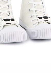 Baskets montantes blanches avec une finition scintillante, dotées de fermoirs en forme de chat avec des lunettes de soleil, et de semelles en caoutchouc texturées avec des nervures.