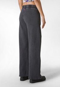 Donkergrijze wijde broek met een elastische tailleband, een gladde textuur en zijzakken, gecombineerd met zwarte schoenen.