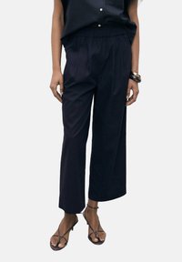 Marineblauwe wijde broek met een elastische tailleband, geplooide voorkant en lichtgewicht stof. Gecombineerd met bruine sandalen met bandjes.