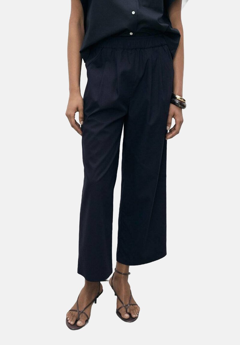 Marineblauwe wijde broek met een elastische tailleband, geplooide voorkant en lichtgewicht stof. Gecombineerd met bruine sandalen met bandjes.
