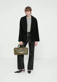 Mulher vestindo casaco preto com golas largas, top cinza, calças de couro pretas, saltos pretos, segurando uma mala de mão verde-oliva com detalhe de estrela.