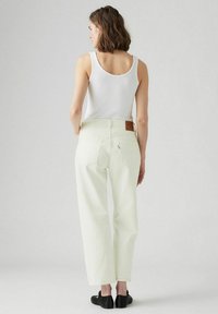 Witte denim broek met een rechte pijp, voorzien van een achterzak en een bruine leren label op de taille. Gedirigeerd met een witte tanktop.