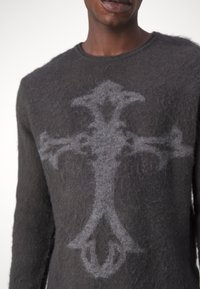 Dunkelgrauer Wollpullover mit strukturierter Oberfläche und einem auffälligen grauen Kreuzdesign auf der Vorderseite. Rundhalsausschnitt und lange Ärmel.