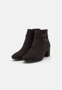 Botas de tobillo de ante negro con tacones de bloque y correas decorativas de doble anillo en los lados exteriores, mostradas sobre un fondo blanco.