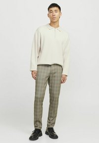Beige ritspullover met een polokraag, gecombineerd met een geruite broek in olijfgroen en beige tinten. De schoenen zijn zwarte veterschoenen.