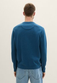 Pulover albastru cu decolteu rotund și mâneci lungi, realizat dintr-un material tricotat texturat. Purtați-l cu blugi albaștri deschis, având un aspect casual.