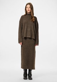 Pull en maille côtelée marron avec un col montant, assorti à une jupe midi. Le mannequin porte des bottines noires. Design simple et texturé.