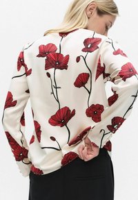 Pitkähihaisen paidan kermanvärinen kangas, jossa suuret punaisen unikon kukkakuviot ja mustat varret. Hihoissa napit, sileä pinta.