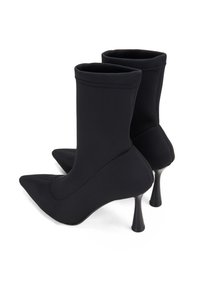 Bottines noires en tissu élastique, avec un bout pointu, une tige ajustée et un talon conique fin. Texture lisse, design minimaliste.