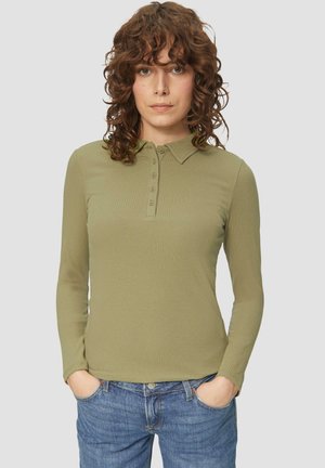 Olijfgroene polo met lange mouwen en een gestructureerd ribbelpatroon, voorzien van een knoopsluiting en een klassieke kraag. Gecombineerd met blauwe jeans.