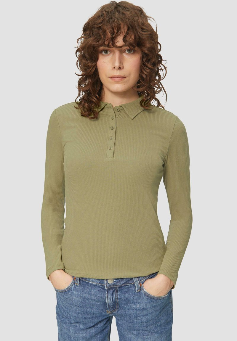 Olijfgroene polo met lange mouwen en een gestructureerd ribbelpatroon, voorzien van een knoopsluiting en een klassieke kraag. Gecombineerd met blauwe jeans.