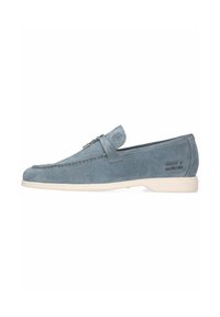 Mocassini in suede blu con superficie liscia, dettagli in cuoio e suola in gomma chiara. Presentano cuciture decorative e un logo sottile.