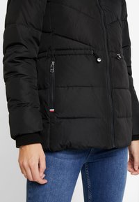 Chaqueta acolchada negra con diseño de colchas, bolsillos con cremallera en contraste, dobladillo con cordón y puños acanalados. Ideal para mantener el calor y para uso al aire libre.