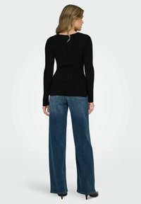 Melna ribota garām piedurknēm augšdaļa ar piegulošu dizainu, apvienota ar platajām kājām tumši zilajiem džinsiem. Apģērbam ir vienkāršs diegs un minimāla aparatūra.