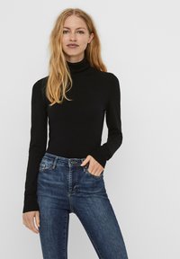 Svart turtleneck-top laget av ribbestrikket stoff, kombinert med tettsittende mørkeblå jeans. Lange ermer med mansjetter, minimalistisk design.