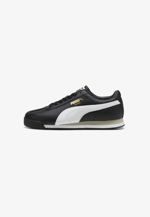 Baskets basses Puma Roma noires avec bande latérale blanche, lacets noirs et logo Puma doré sur le côté. Semelle blanche et beige avec semelle extérieure noire.
