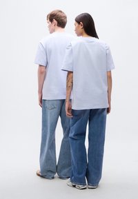 Ανοιχτό μπλε, υπερμεγέθη μπλουζάκια με κοντά μανίκια, συνδυασμένα με φαρδιά μπλε τζιν. Ομαλή υφή βαμβακιού με μινιμαλιστικό σχέδιο.