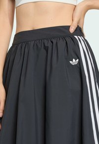 Čierny šortkový sukňový model s širokým pásom, ktorý má biele pruhované akcenty a vyšívané logo. Tkanina je hladká a mierne lesklá.