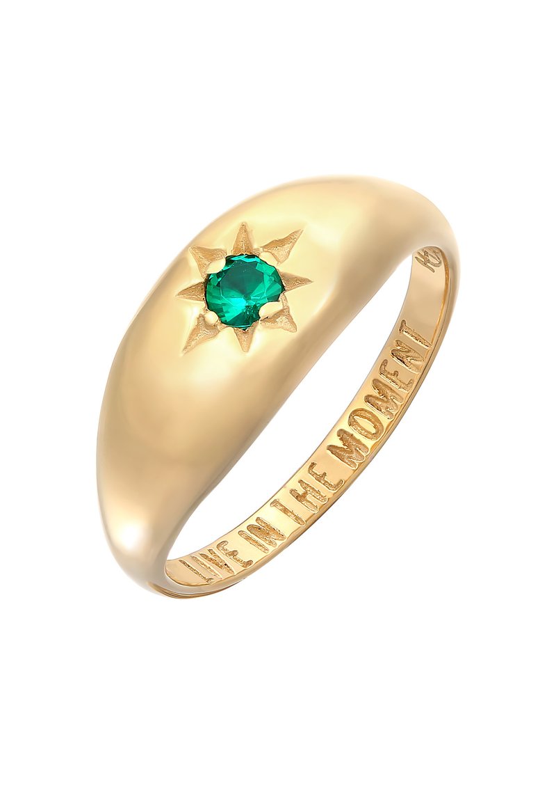 Guldring med en slät, rund band som har en grön ädelsten i mitten, omgiven av en solstråle-design. Graverad inuti: "LEVA I ÖGONBLICKET."