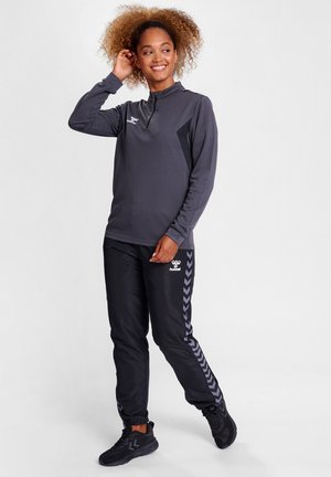 Sporty sæt bestående af en grå langærmet top med halv lynlås og sorte bukser med et chevron-mønster på siden. Fremstillet af glat, letvægtsstof.