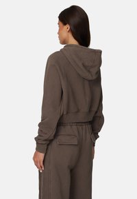 Haut à capuche brun coupé, fabriqué en tissu doux. Doté de poignets côtelés et d'une coupe décontractée, associé à un pantalon à cordon de serrage assorti.