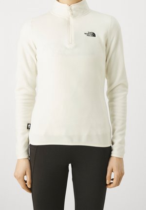 Biały polar z długim rękawem, półzamkiem i czarnym logo „The North Face” na piersi, noszony z czarnymi spodniami.