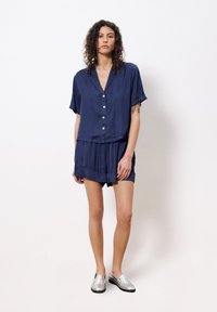 Navyblaues kurzärmeliges Hemd mit Knöpfen und Kragen, kombiniert mit passenden hoch taillierten Shorts aus glattem Stoff; dazu silberne Loafers.