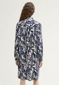 Langdurige shirtjurk met een opvallend zwart-, wit-, blauw- en roze abstract patroon; lichtgewicht stof; rechte snit; knoopjes aan de voorkant.