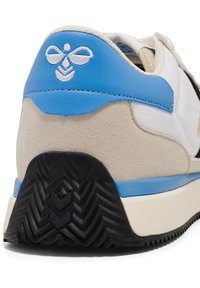 Sneaker med en blå läderhättan, ovandel i beige mocka, vit meshpanel och svart gummisula med zigzag-mönster.